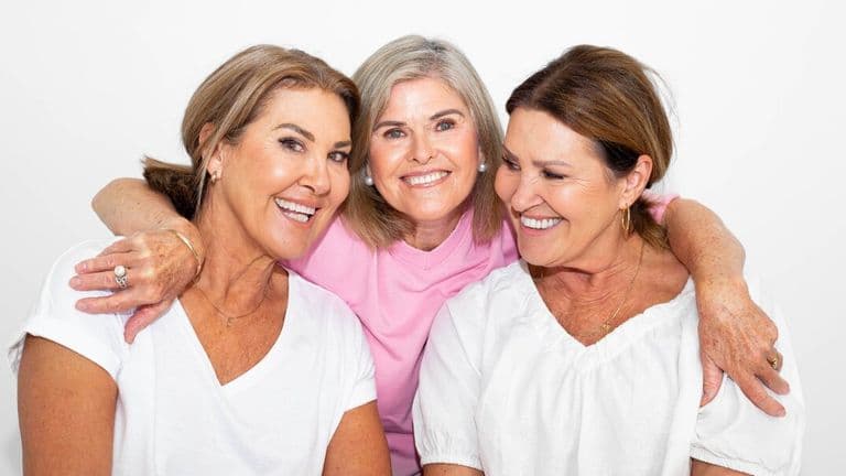 Three women smiling together, representing confidence, inclusivity, and accessible beauty.