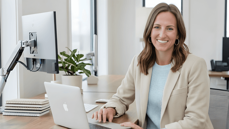 Professional woman smiling at her desk with a laptop in a modern office setting.