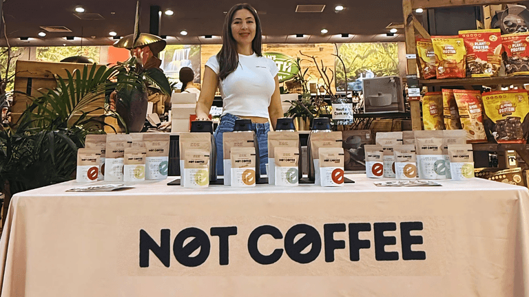Founder Sila Gatti at a Not Coffee display table showcasing caffeine-free products in a health food store.