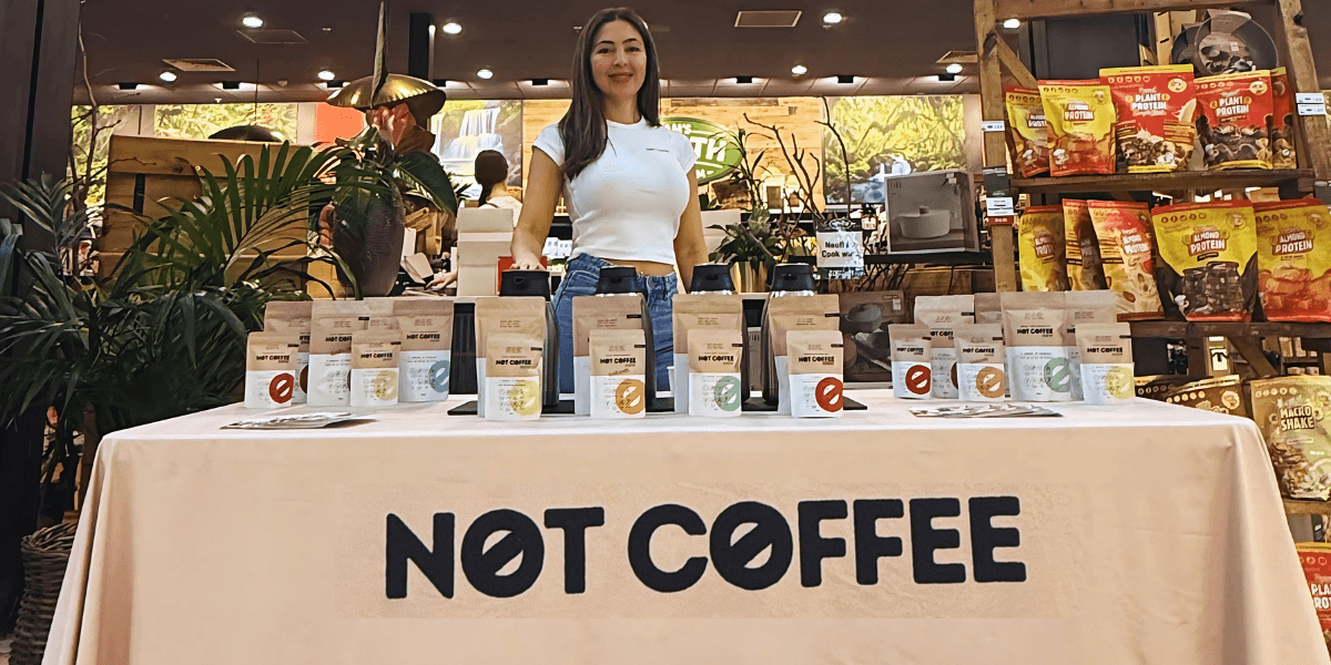 Founder Sila Gatti at a Not Coffee display table showcasing caffeine-free products in a health food store.