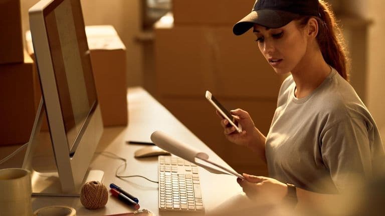 Young Delivery Woman Using Mobile Phone While Going Through Dispatch List Office 637285 6319
