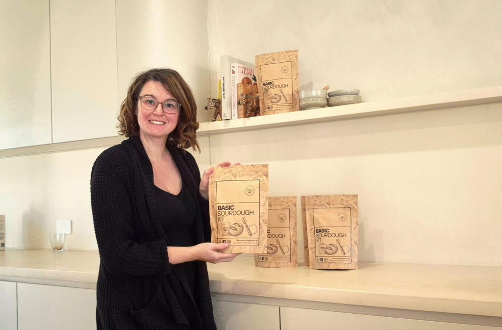 Woman holding a Basic Sourdough Kit with additional kits displayed on a kitchen counter.