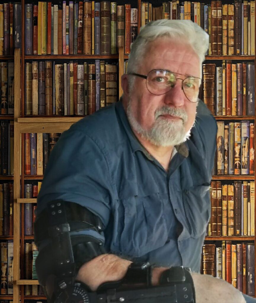 Baer Charlton seated before bookshelves wearing an arm brace.