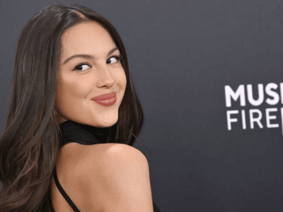 Young woman in black dress poses playfully against a dark backdrop with event branding