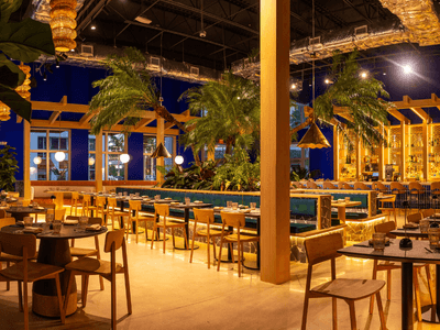 Modern restaurant interior with wooden furniture, tropical plants, and warm lighting